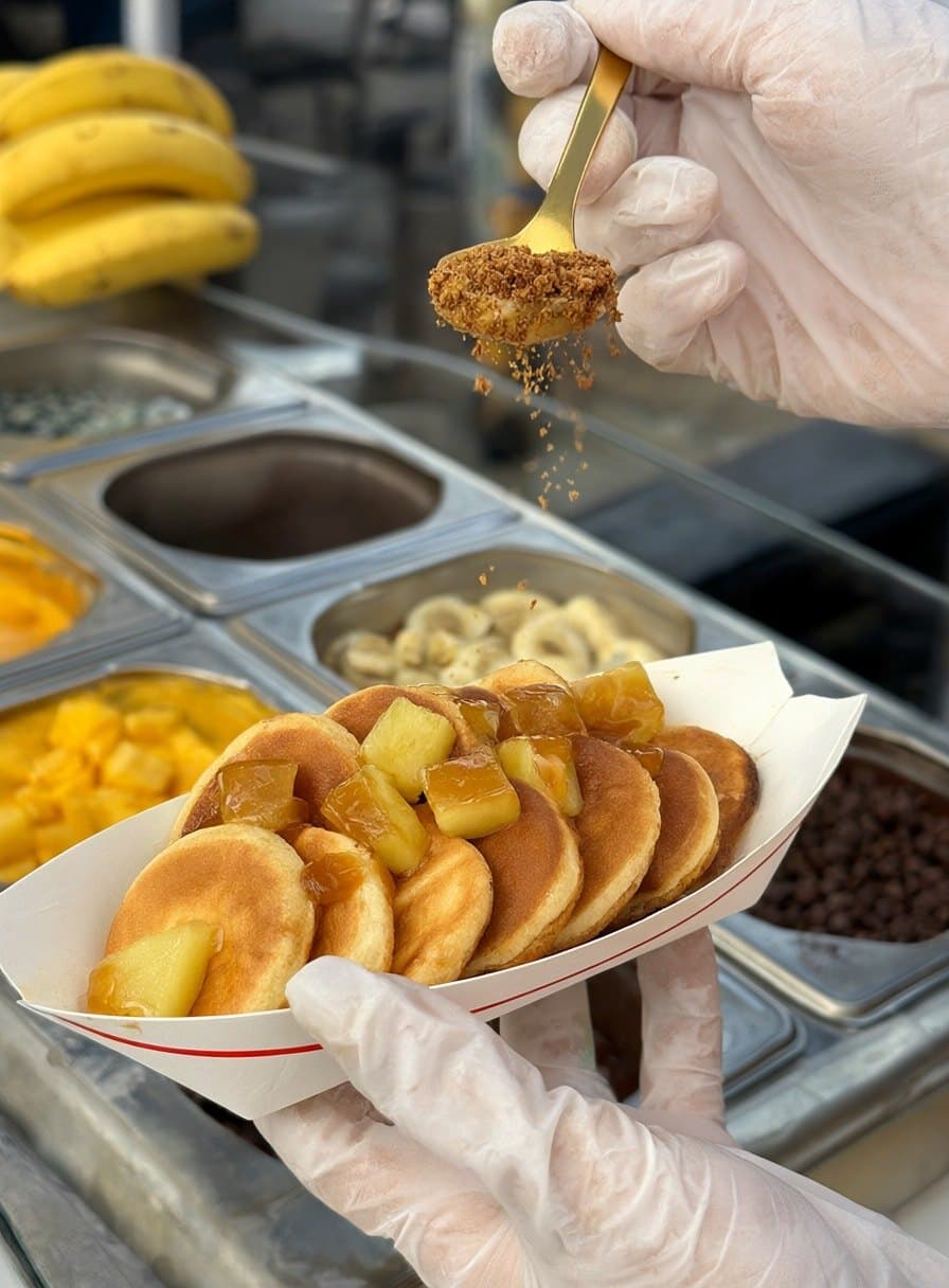 Au bar, des mini pancakes au caramel et à l’ananas reçoivent leur topping de spéculoos