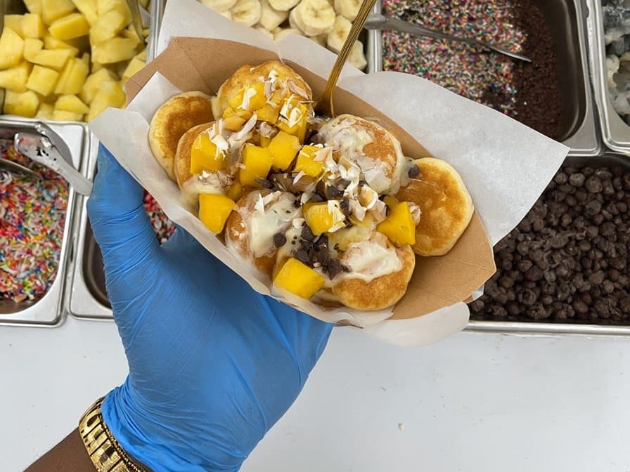 Mini pancakes au chocolat blanc, mangue et coco, devant le bar à toppings